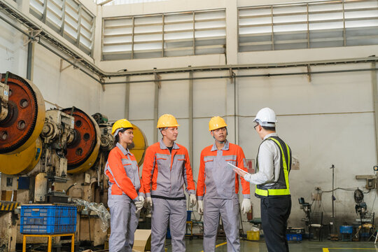 Team of factory workers in conversation with engineer near multiple industrial punch press machines