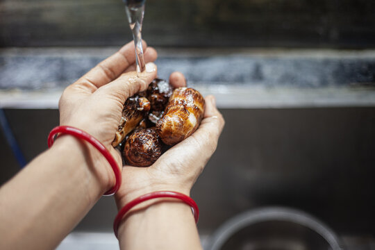 Indian female hands washing boiled taro roots under running water