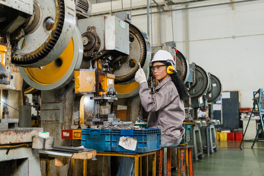 Female machine operator holding stamped metal part beside open power press die