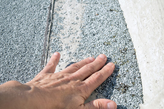 Flat roof granule loss inspected by roofer. Bare spot on aged modified bitumen cap sheet at concrete parapet edge. UV degradation risk. 2-ply SBS or modified bitumen roofing system. Selective focus.