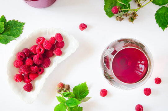 Top view of raspberries and a glass of red wine on a white background