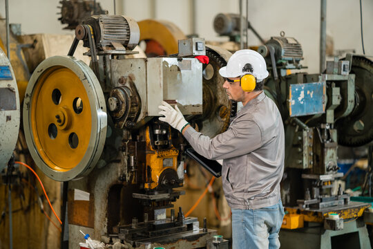 Factory engineer inspecting power press control housing while holding a tablet