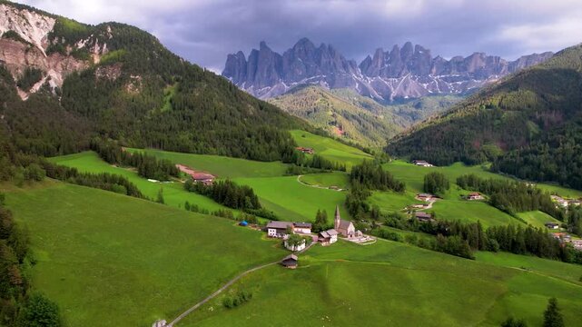 Cinematic Sunset Drone Pan Reveal of Santa Maddalena Village and Iconic Alpine Chapel in Val di Funes Dolomites Italy Majestic Odle Peaks and Green Meadows Golden Hour Aerial Footage