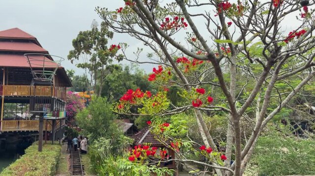 Exotic tropical resort with traditional wooden architecture, vibrant red flamboyant flowers, and lush green foliage.