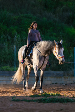 Girl riding grey horse in outdoor paddock