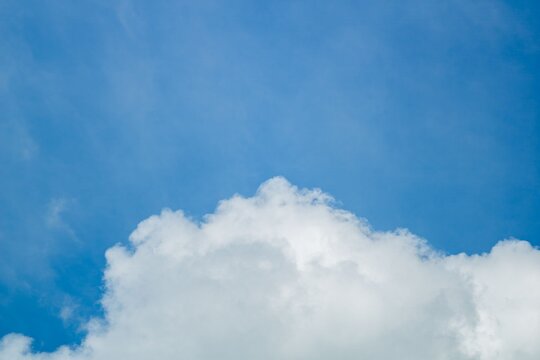 Dramatic fluffy white cloud formation in clear blue sky. Soft cumulus texture floating above landscape for weather or nature backdrop.