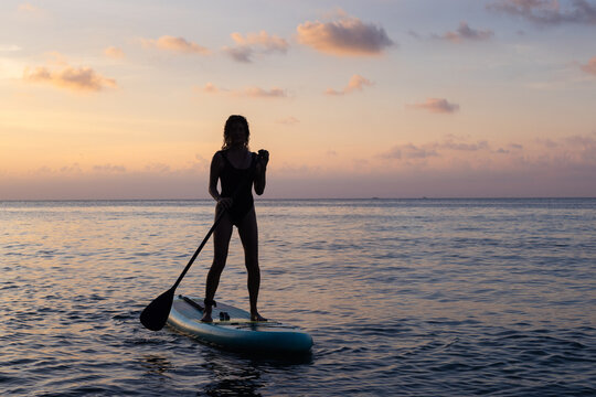 silhouette of woman on SUP on sunset beach, summer holidays activity