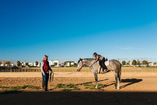 Equestrian instructor teaching girl riding dapple gray horse
