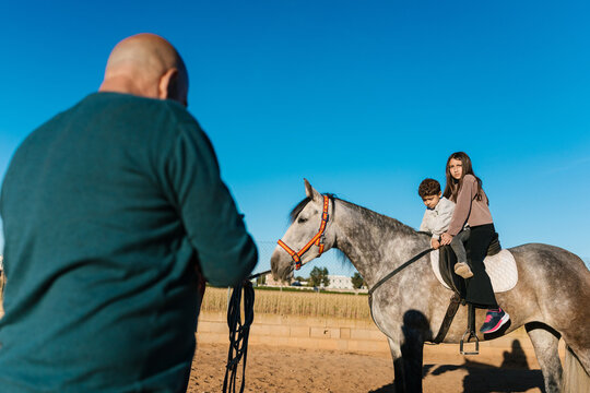 Instructor teaching children riding horse lessons outdoors