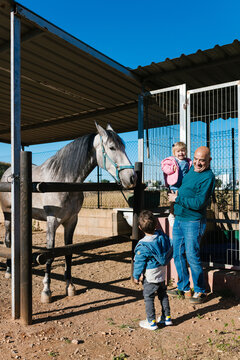 Grandfather and grandchildren interacting with horse in stable