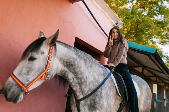 Young girl riding dappled horse making peace sign