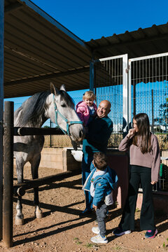 Grandfather and grandchildren interacting with horse at farm