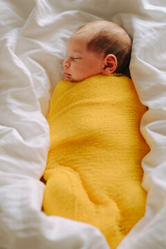 Newborn baby swaddled in yellow fabric lying of soft white bedding