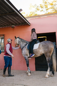 Adult teaching child horseback riding lesson