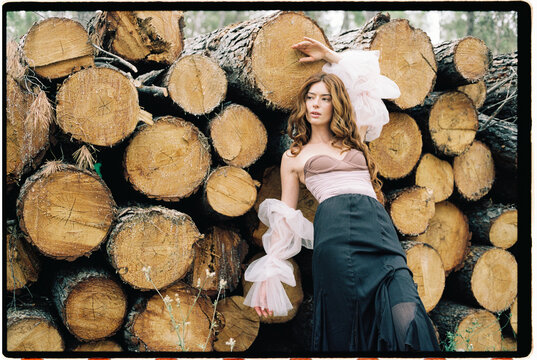 Woman posing against stacked wood logs