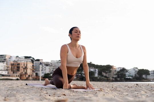 A woman with her eyes closed practicing yoga on the beach at sunset