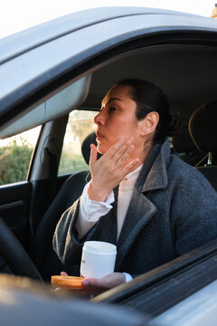 A woman applying skincare to herself in the car at sunset