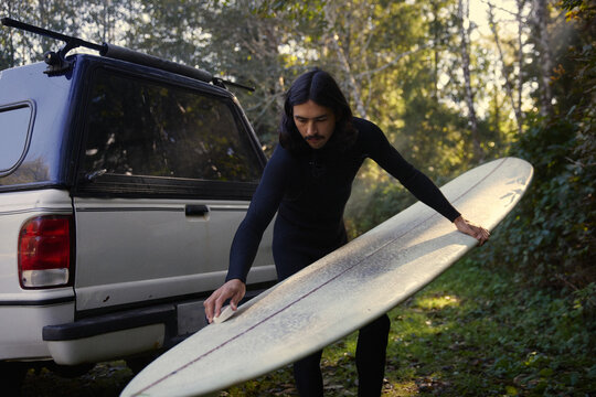 Surfer stands by truck before surfing in the forest