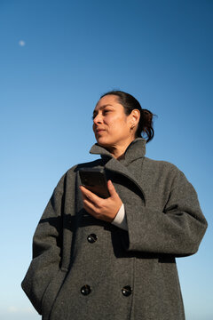 Woman Holding Phone and Looking at Sky in Clear Weather