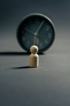 Wooden figurine waiting in front of a clock as a concept of time, patience and deadline