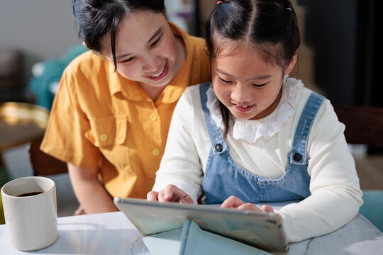 Woman and daughter using digital tablet together, smiling.
