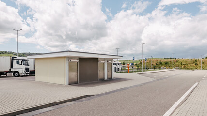 Naklejka premium ruck Parking Area with Sanitary Facility, White Trucks, and Cloudy Sky, Modern Rest Stop, High-Quality Commercial Photography