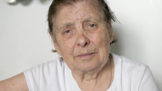 Elder 90 year old woman with wrinkled skin and sad eyes looks at camera. Portrait elderly woman in close up on white background. Spots of vitamin and mineral deficiency are visible on skin old person