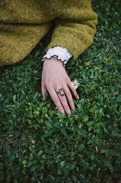 Hand resting on grass, holding flower while wearing ring