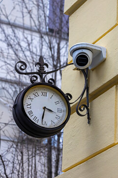 Old public clock in urban city street with cctv camera on building facade