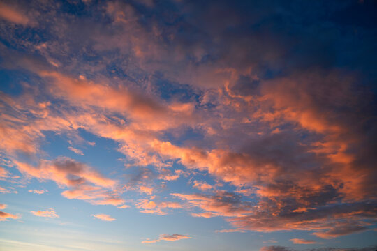 Vivid colors illuminate soft clouds floating across a vast horizon as the sun sets, creating a peaceful and calm atmosphere in the cooling evening air