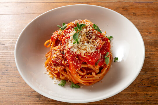 Traditional Umbrian stringozzi pasta with tomato sauce, grated Pecorino cheese and fresh herbs served in a white bowl on a rustic wooden table.