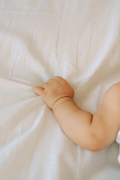 Close-up of baby's hand gently grasping a white bed sheet