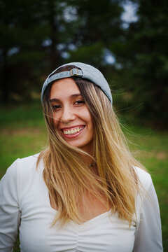 portrait of a young Latino brunette girl wearing a blue backwards baseball cap, Jeans and a white shirt, smiling at the camera
