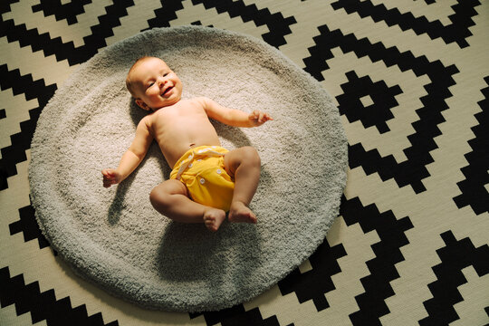 Smiling baby in yellow cloth diaper on round mat