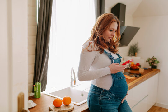 Pregnant female with smartphone in the kitchen 