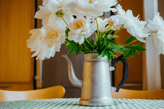Flowers in a kettle on a table in a kitchen setting