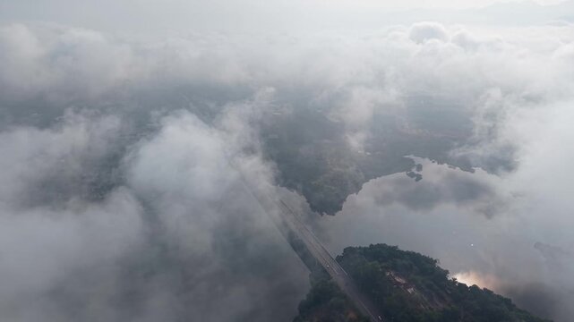 An aerial shot capturing a road cutting through a dense fog in a lush natural landscape at Tasik Raban