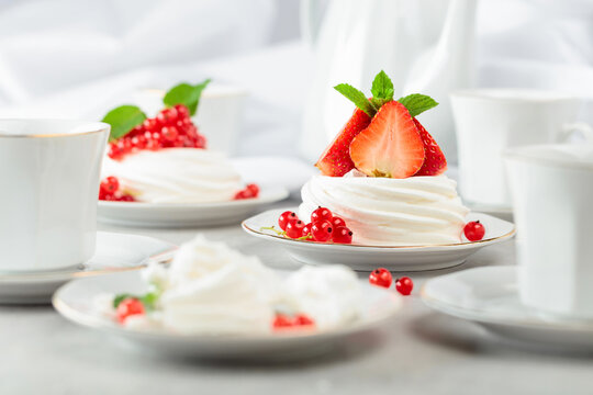 Pavlova dessert with strawberries, red currant, and mint on a white table.