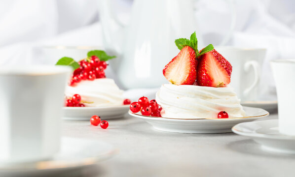 Pavlova dessert with strawberries, red currant, and mint on a white table.