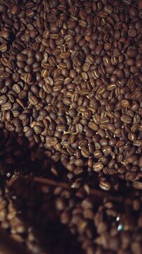 coffee beans roasting process closeup, professional roaster machinery equipment roast brown and golden colored cafe seeds close-up, directly above top view, 4k vertical video