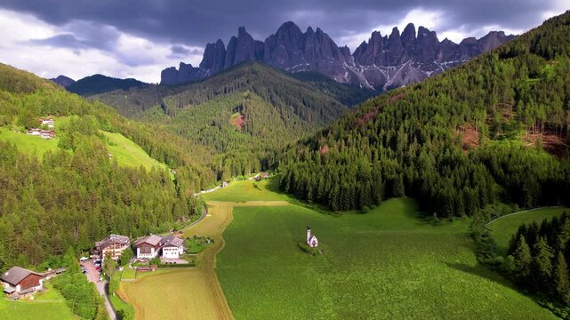 Val di Funes Dolomites Italy 4K Drone. Sideways tracking aerial flight over lonely San Giovanni in Ranui church in green alpine meadow with mountain peaks background cinematic travel stock video