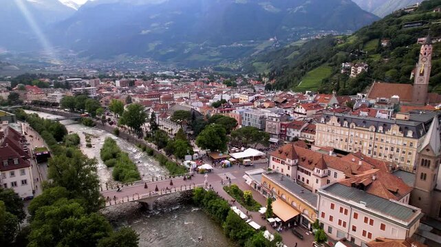 Cinematic Sunset Drone Reveal of Merano Spa Resort Cityscape South Tyrol Italy Sun Rays Piercing Through Alpine Peaks Overlooking Historic Center and Passer River Bridge 4K Footage