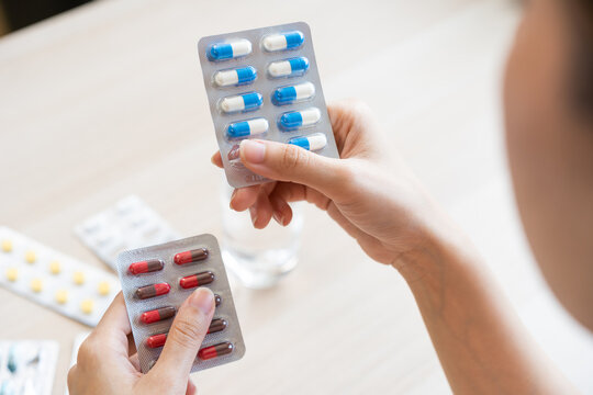Health care treatment asian young woman holding capsules medicine pack reading label text about medical information instructions side effects at medicine on table at home, pharmacy medicament concept.