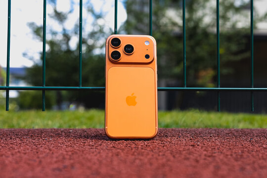 KYIV, UKRAINE - July 10, 2026 : Apple iPhone 17 Pro in Cosmic Orange color leaning against a green wire fence on a red running track, outdoor sport concept.
