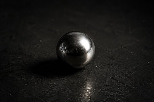 Reflective silver ball bearing on a dark surface with dramatic side lighting.