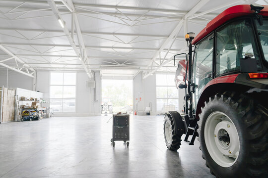 Modern agricultural tractor in spacious service workshop, professional farm equipment maintenance, industrial repair facility with copy space, agriculture technology.
