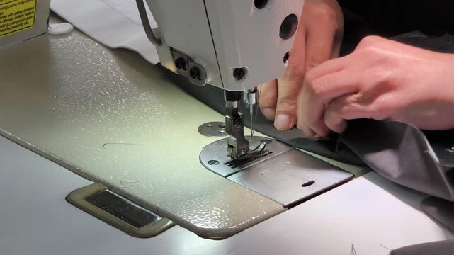 Close up of tailor hands working with industrial sewing machine, stitching fabric in garment factory