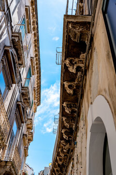 A view from below of a long balcony on an ancient Sicilian stone palace, showing its rich Baroque decorations