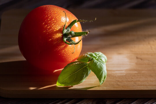 Fresh Ripe Tomato with Basil Leaves on Wooden Cutting Board, Minimalist Still Life