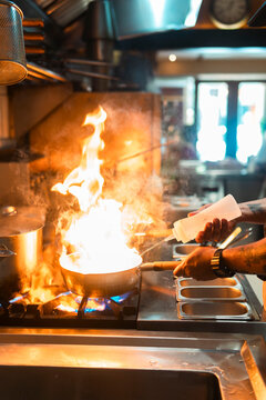 Culinary Mastery in Action: A chef's skilled hands orchestrate a fiery culinary creation in a professional kitchen, showcasing the intense heat and dynamic atmosphere of a busy restaurant.